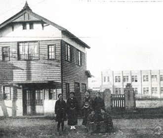 創立当時の正門、正面奥に木造2階建校舎、左建物は生徒の寄宿舎